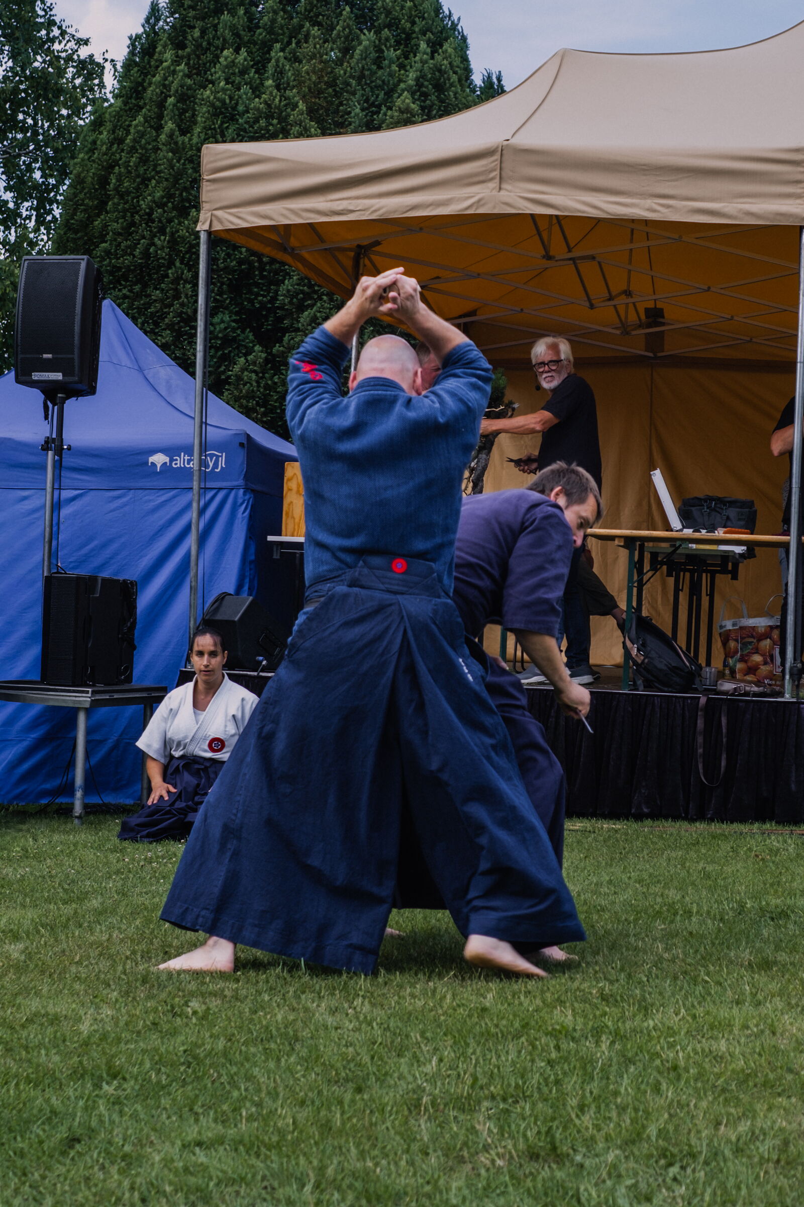 Venkovní ukázka Hiko-ryu Taijutsu u pódia — cvičenec se zbraní nad hlavou, soupeř s nožem